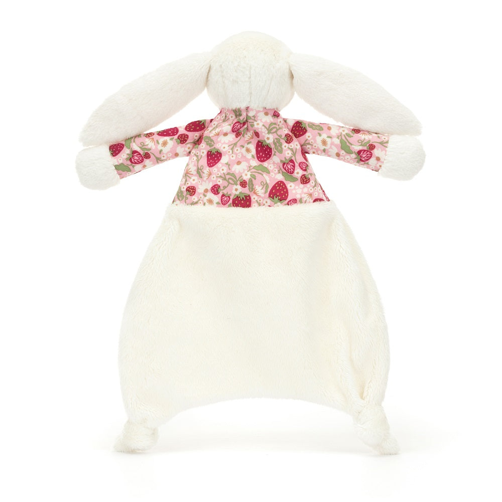 A stuffed bunny with a floral and strawberry print shirt and a white blanket.