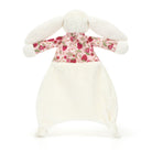 A stuffed bunny with a floral and strawberry print shirt and a white blanket.