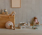 A collection of stuffed animals and toys displayed on a wooden floor, including a unicorn, a mouse family on a suitcase, a rabbit doll, a giraffe, and a doll on a bed.