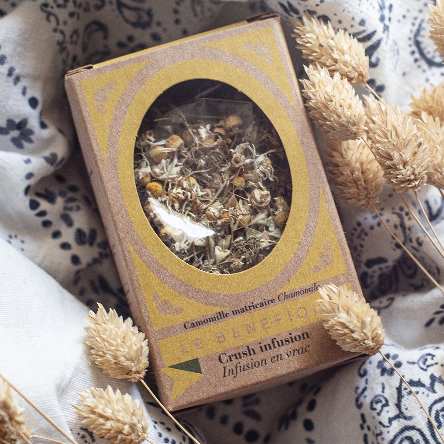 Box of chamomile tea with sprigs of dried grain on paisley fabric.