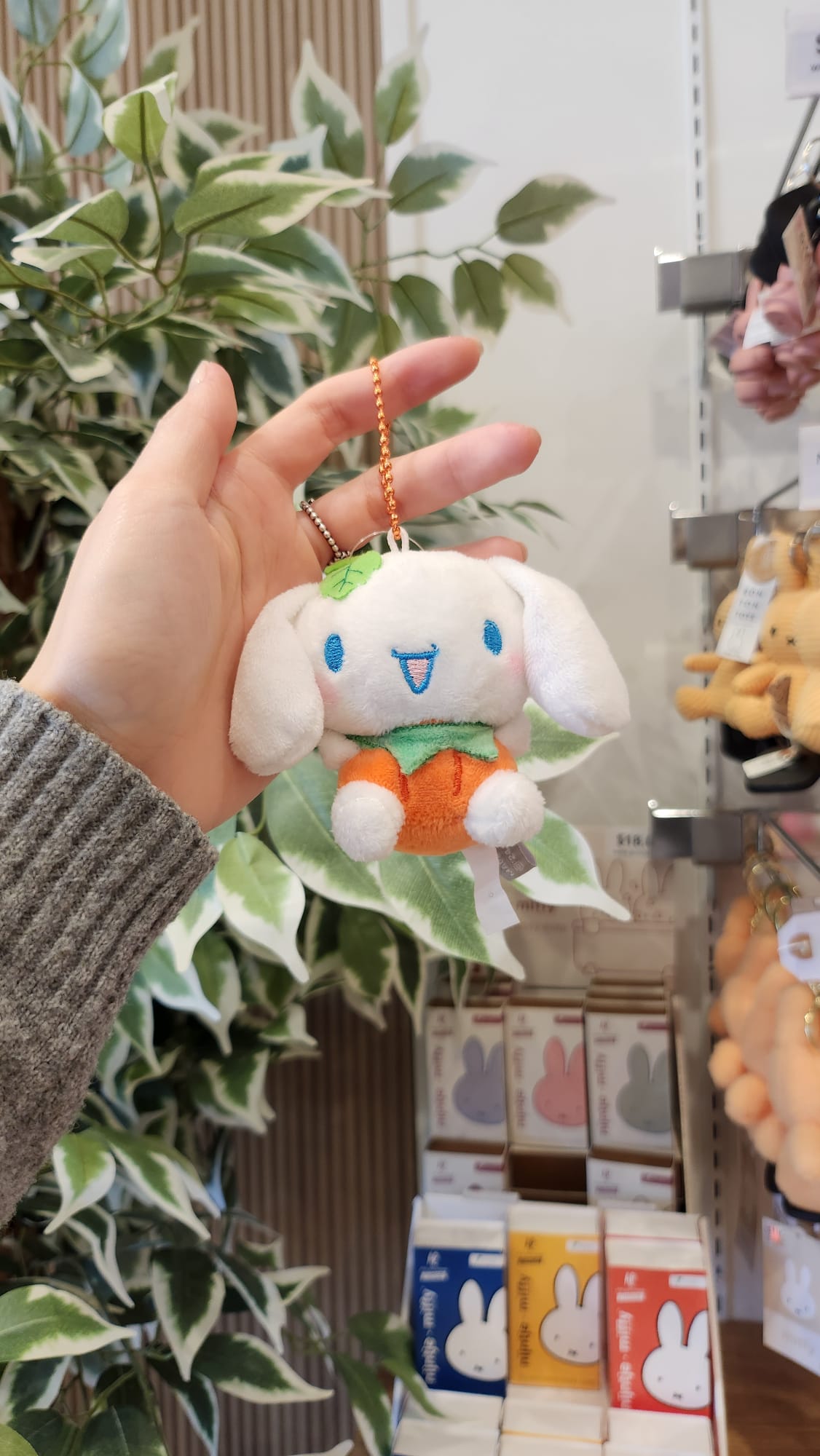 Close-up of a hand holding a white plush keychain with a pumpkin-shaped body, displayed in a store.