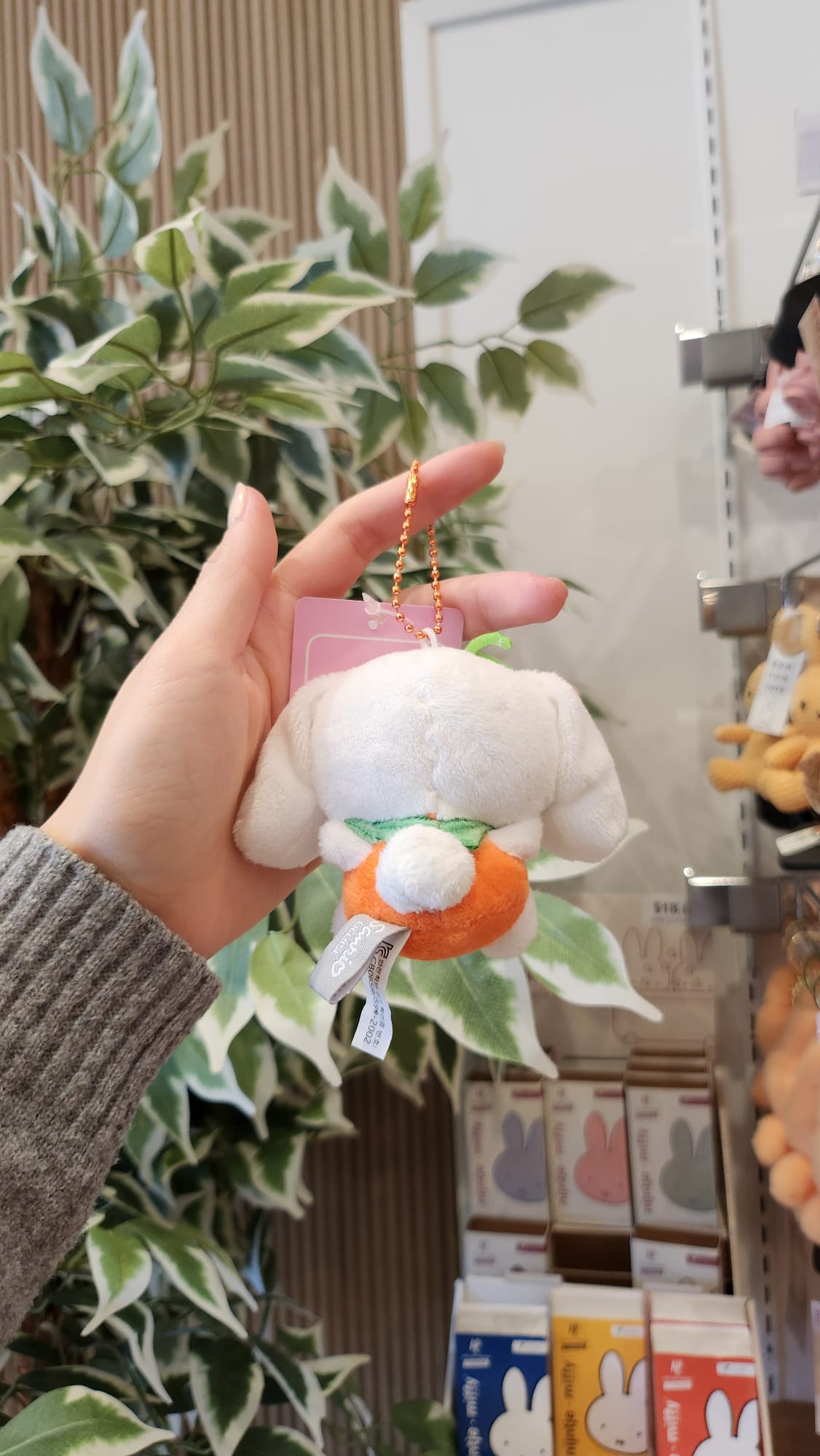 Hand holding a white, plush bunny keychain dressed as a pumpkin.