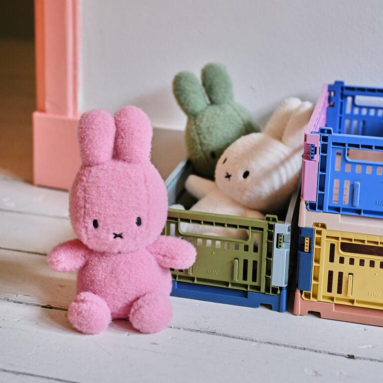 Eye-level shot of three plush bunny toys in colorful storage crates. The bunny in the front is pink, and the two behind it are green and white.