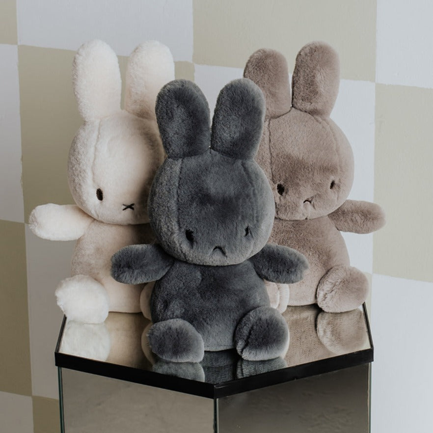 Three plush rabbit toys in white, gray, and beige sitting on a mirrored surface against a checkered background.