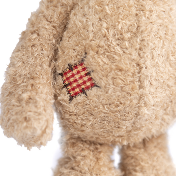 Close-up of a beige teddy bear with a red and yellow patch on a white background