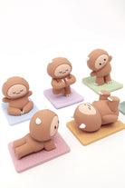 Five brown cartoon figurines in yoga poses on colorful mats.