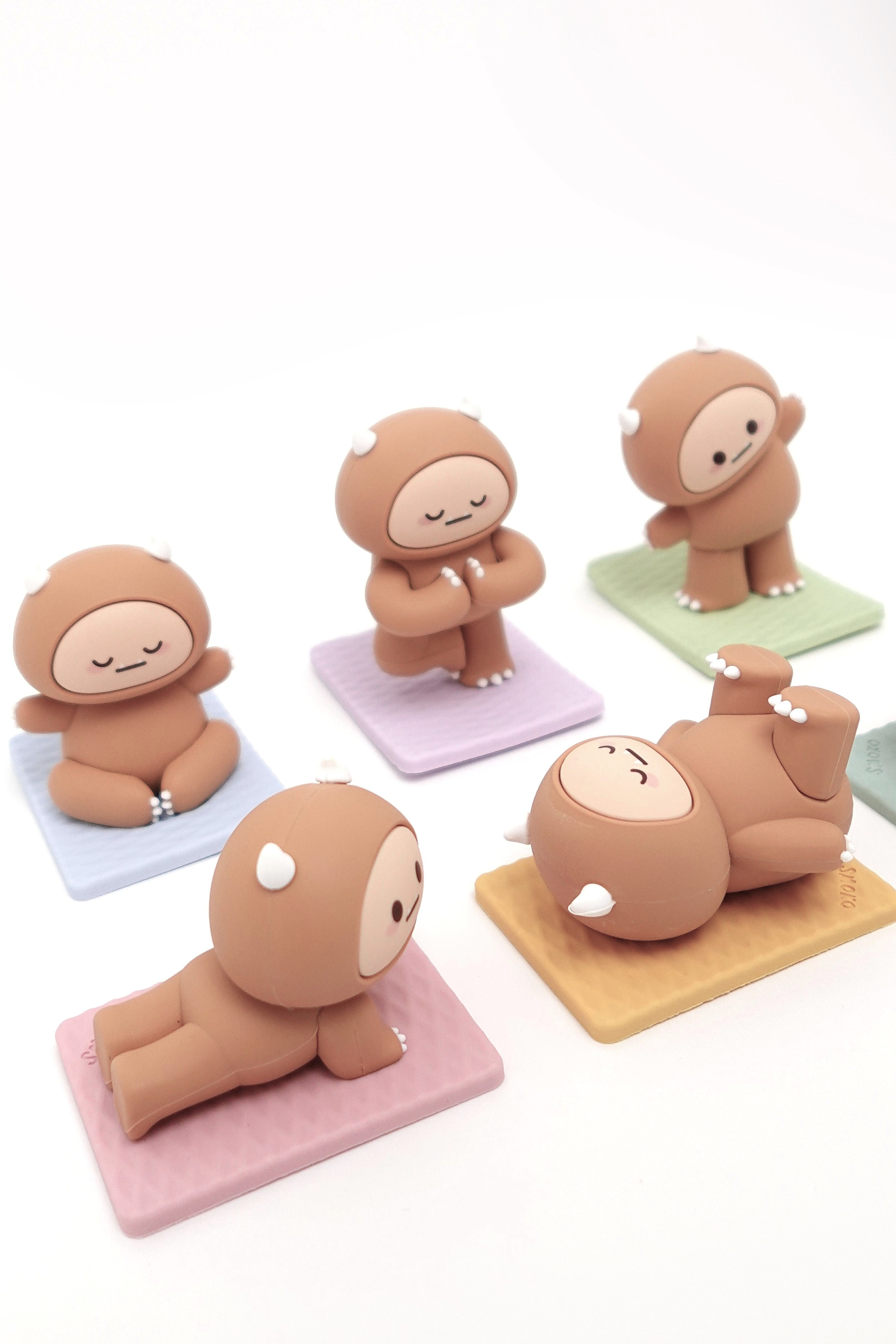 Five brown cartoon figurines in yoga poses on colorful mats.
