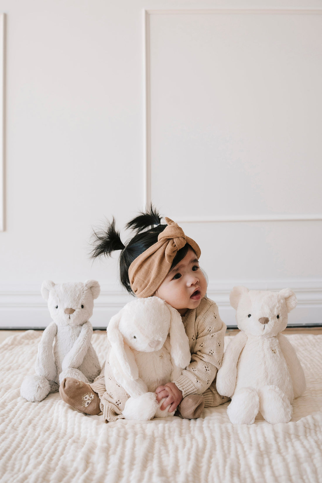 Baby girl in beige outfit with stuffed animals.