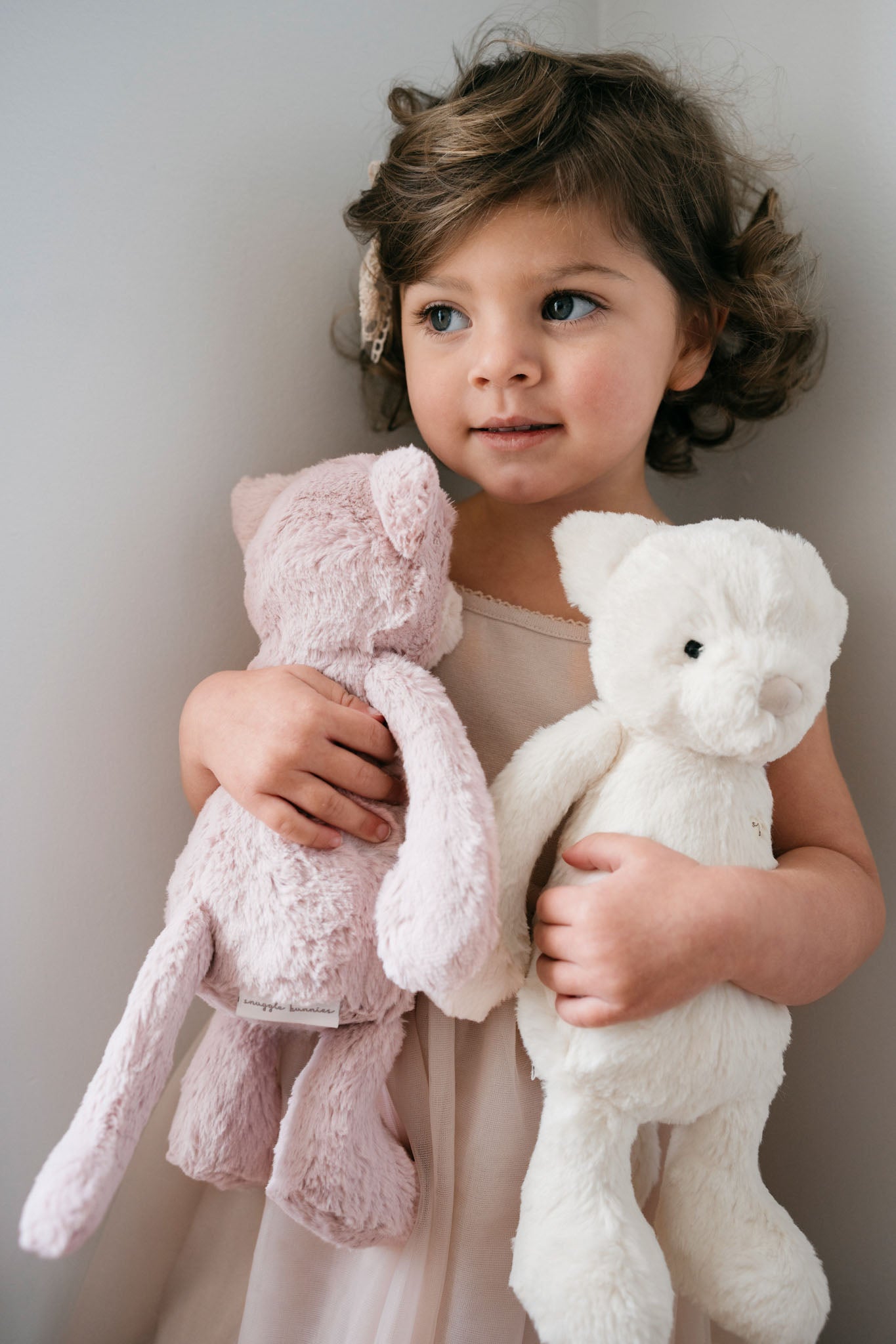 Girl holding pink and white plush animals.