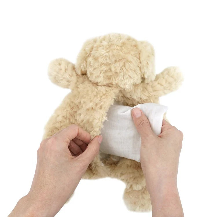 Tan stuffed dog with opening on chest, hands inserting white pouch.