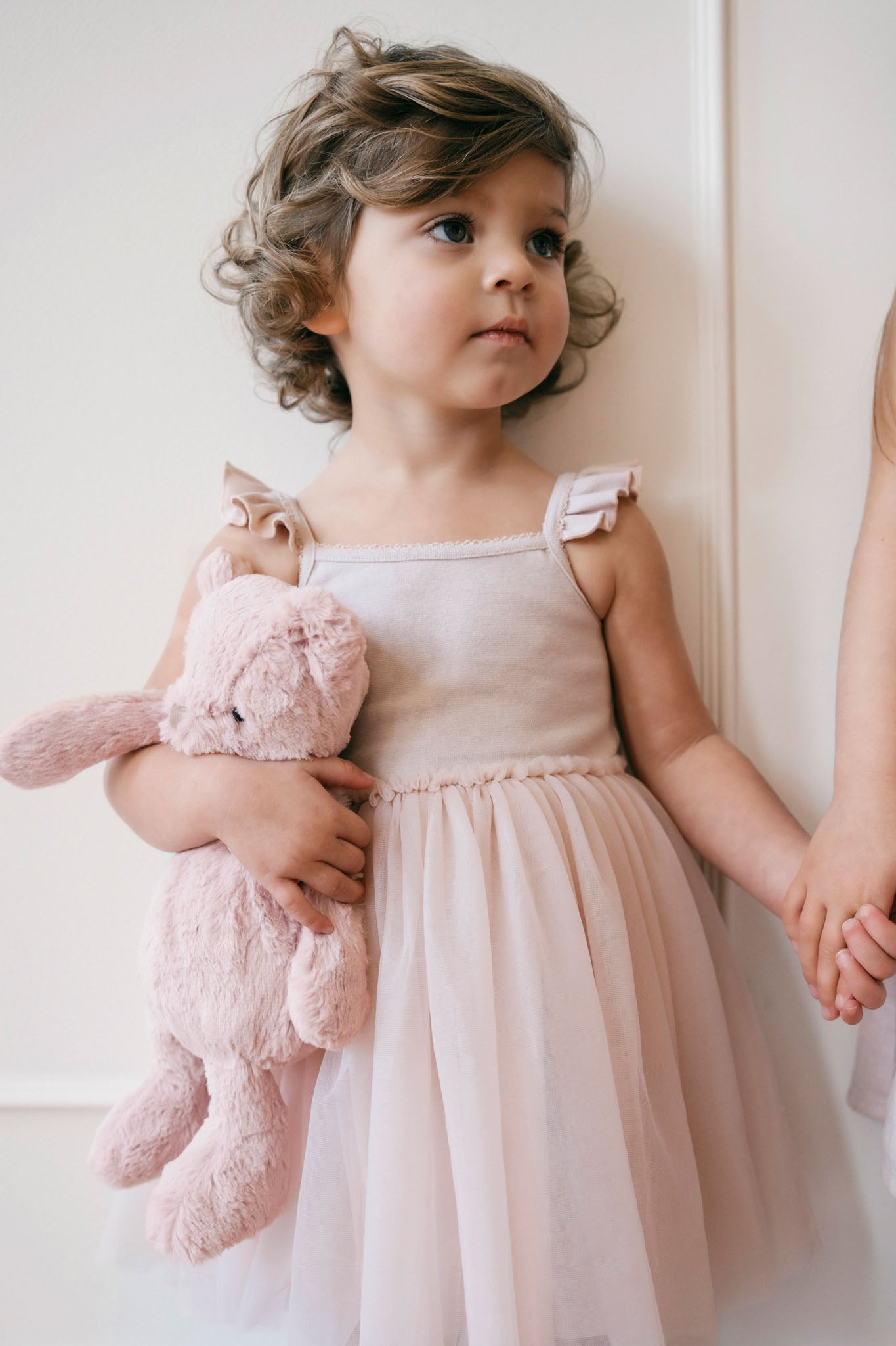 A little girl in a pink dress holds a pink bunny while holding hands with another child.