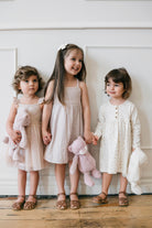 Three young girls in dresses and sandals, holding stuffed animals.