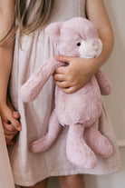 Child in pink linen dress holding a pink plush bunny.