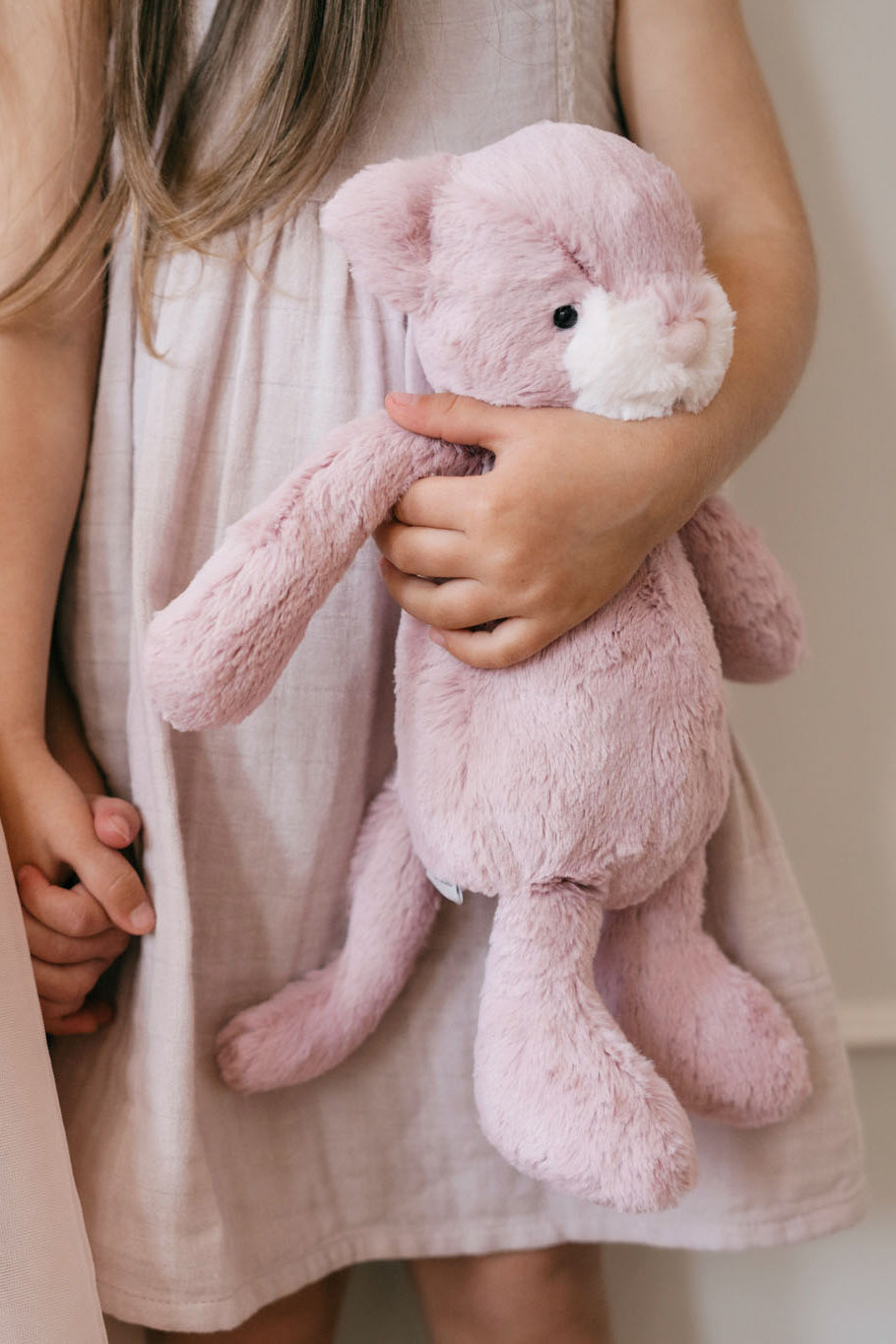 Child in pink linen dress holding a pink plush bunny.