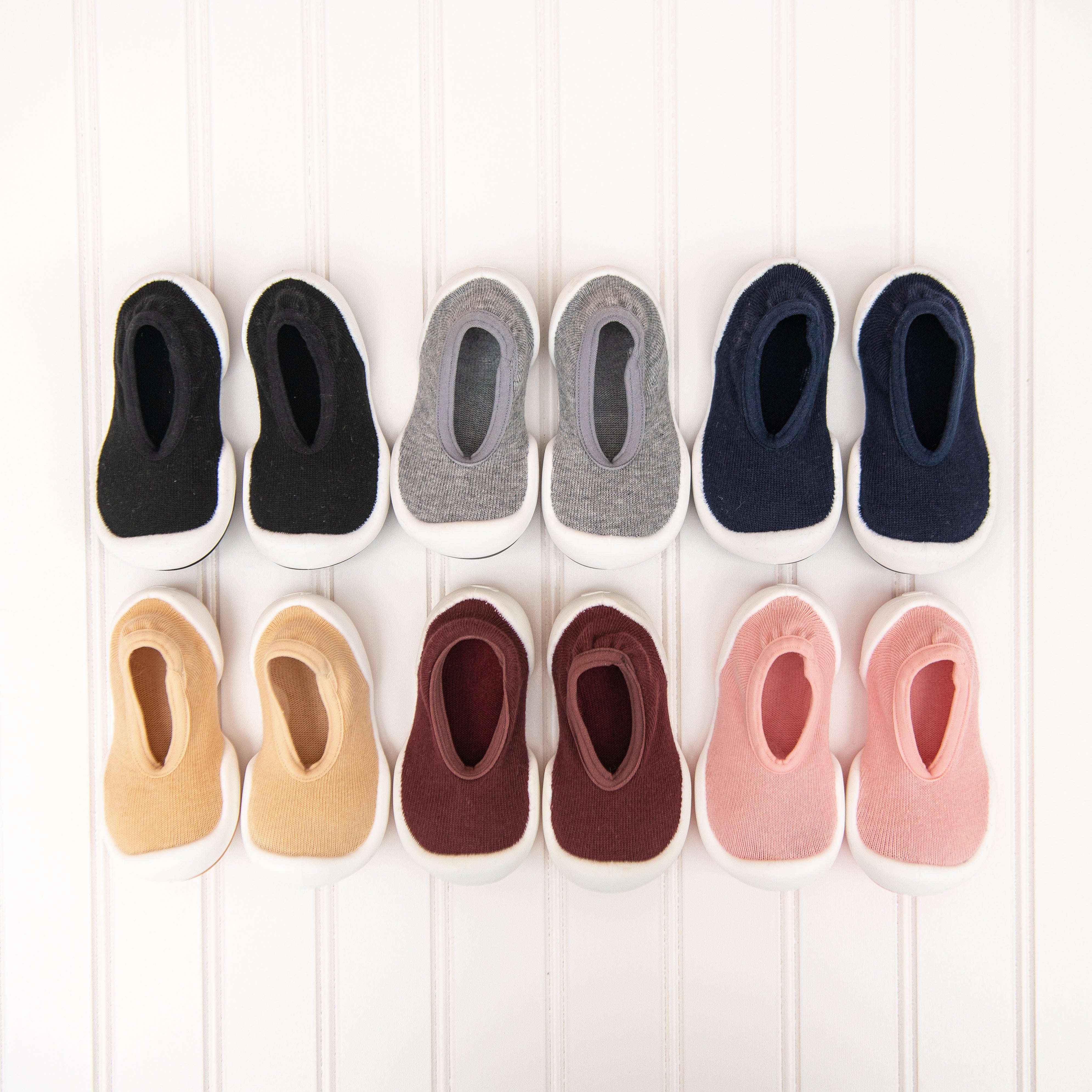 Ten baby shoes in different colors on a white paneled surface.