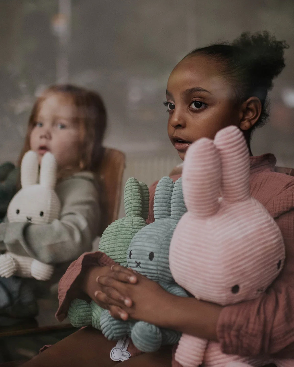 Two children holding plush toys in a cozy indoor setting