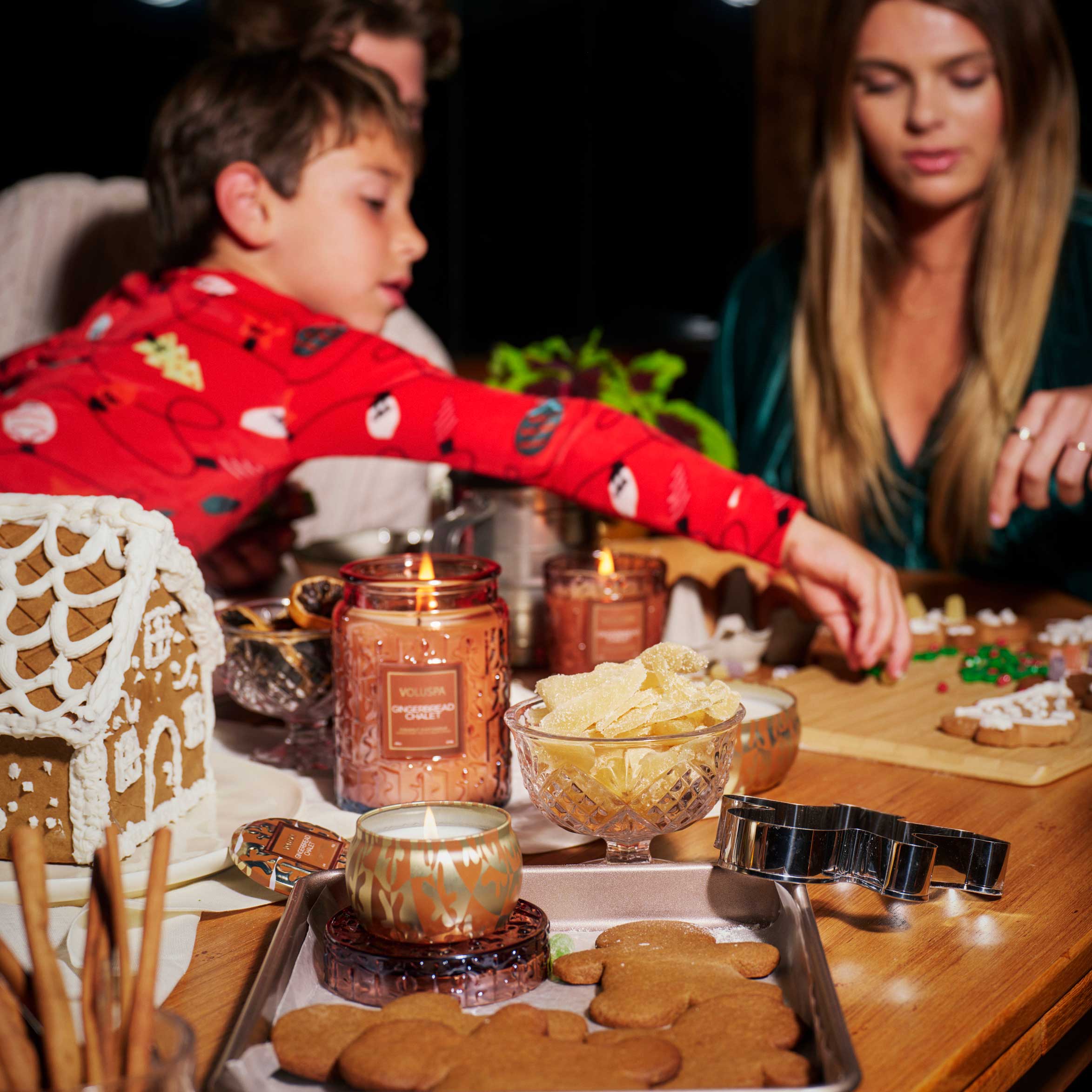 Family gathered around a table with gingerbread house building materials and a candle.