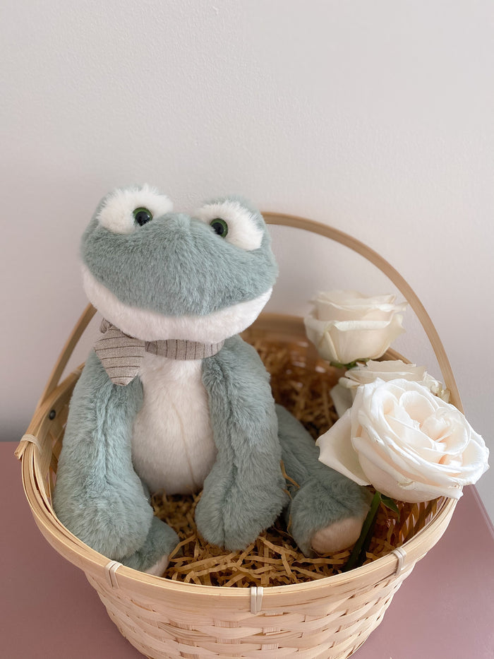 Stuffed blue frog in a basket with white roses.