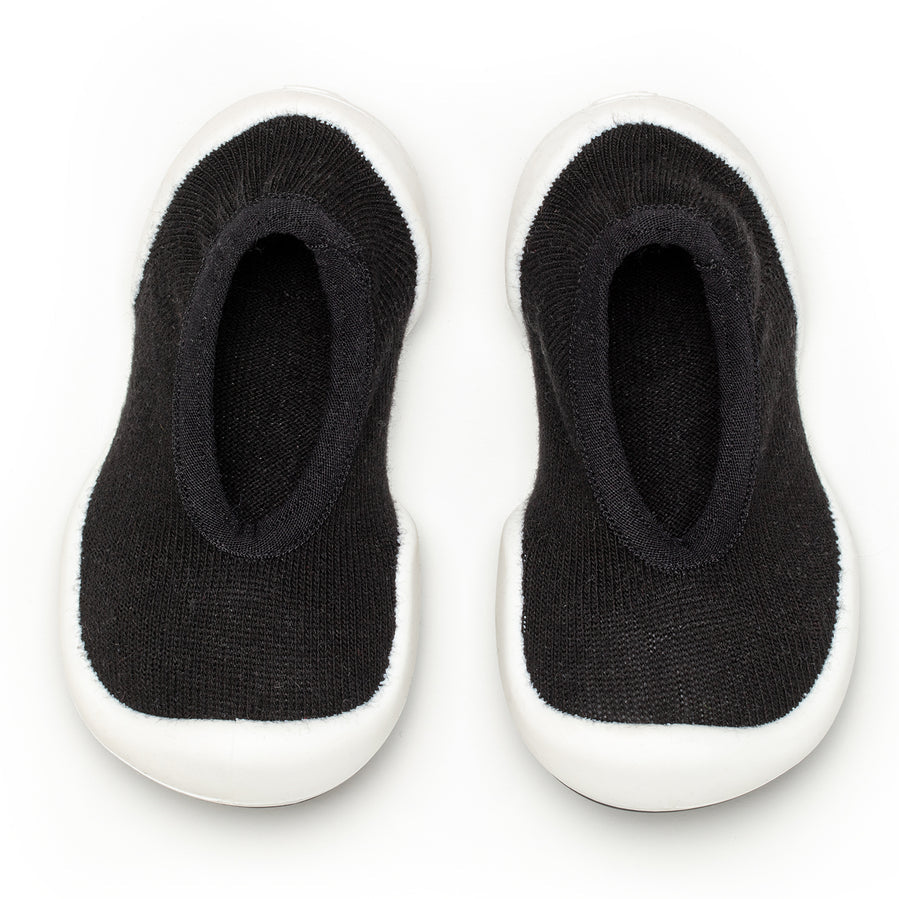 A pair of black sock shoes with white soles.