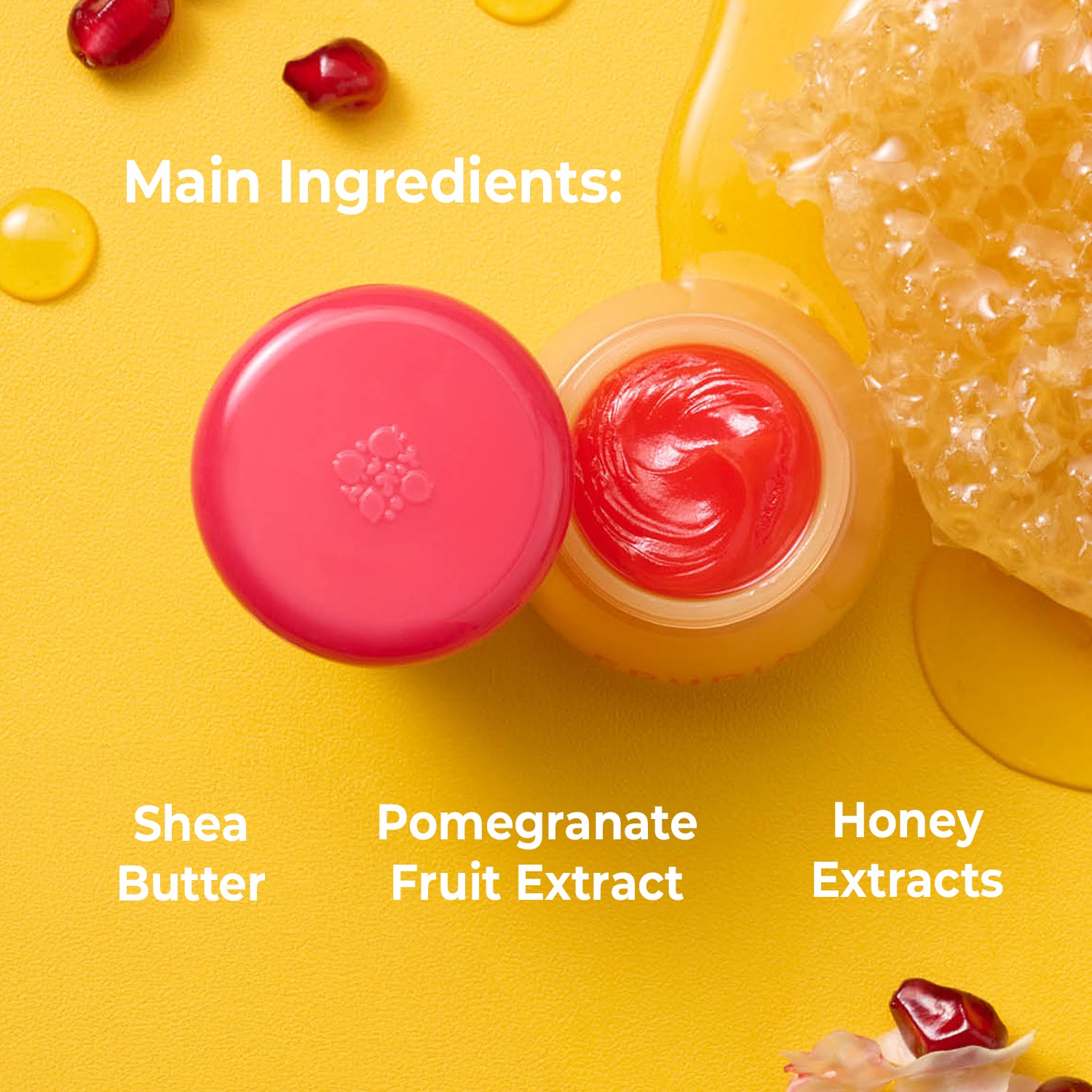 Product image highlighting the main ingredients: shea butter, pomegranate fruit extract, and honey extracts. The image features two small containers, one with a red lid and the other with a yellow, containing a red balm. Honeycomb and pomegranate seeds are featured in the background.