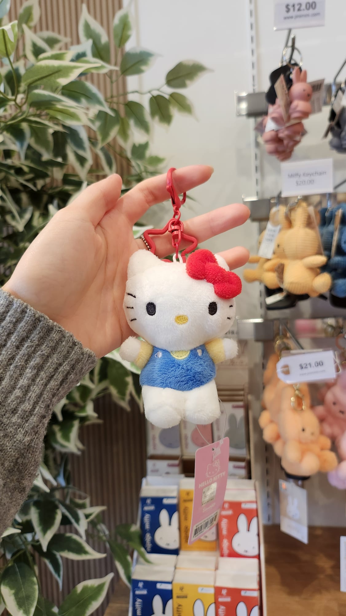 A person holding a Hello Kitty plush keychain with a red bow.
