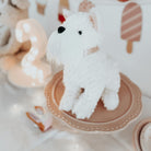 White stuffed dog on a pink plate, with a lit number two and toy cake in the background.