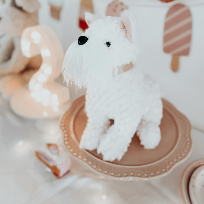 White stuffed dog on a pink plate, with a lit number two and toy cake in the background.