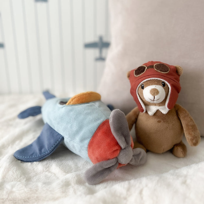 Plush toy airplane and teddy bear with aviator hat on a soft surface