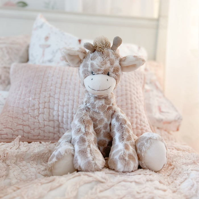 Stuffed giraffe toy sitting on a pink bed.