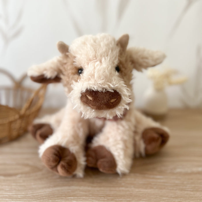 Cream and brown stuffed cow sitting on a wood surface.