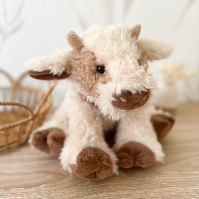 Stuffed cow toy with light brown and cream fur sitting on a wooden surface.