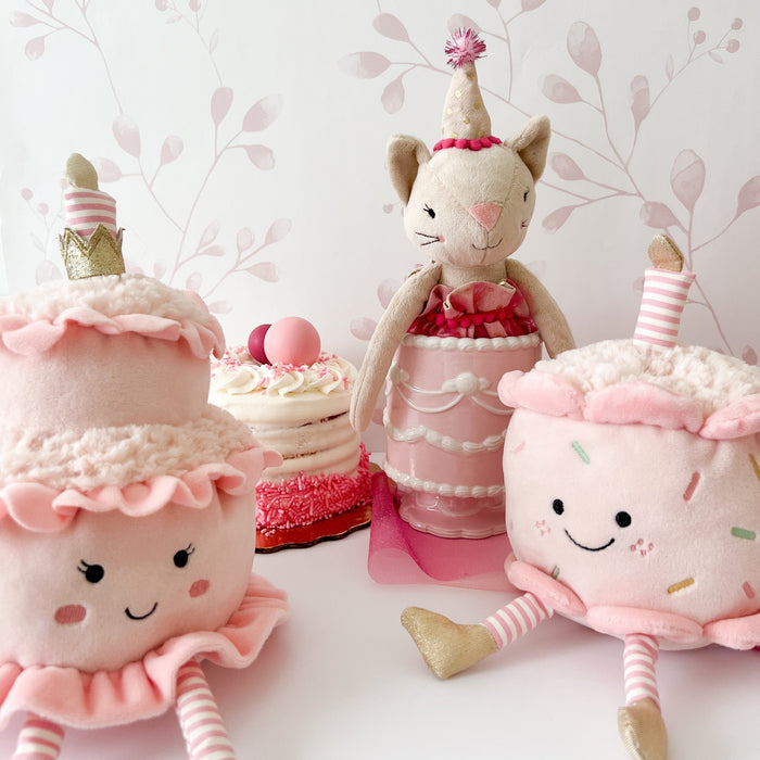 Plush toy cats and cakes in front of a pink and white floral wallpaper.