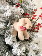 Tan plush puppy ornament with red polka-dot bandana hanging on a snow-covered Christmas tree.