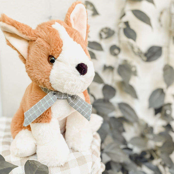 Stuffed brown and white dog with plaid bow tie, sitting.