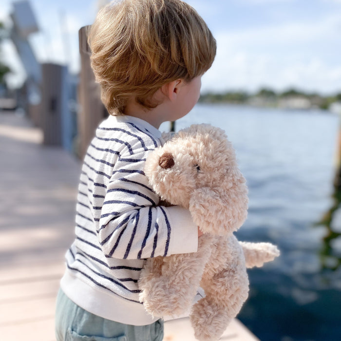 Child in striped shirt holding a plush dog toy on a dock.