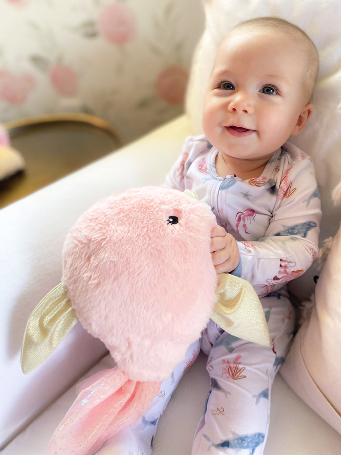 A baby in patterned pajamas sits holding a pink stuffed animal.