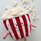 A plush popcorn toy with red and white stripes, a smiling face, and striped arms and legs.