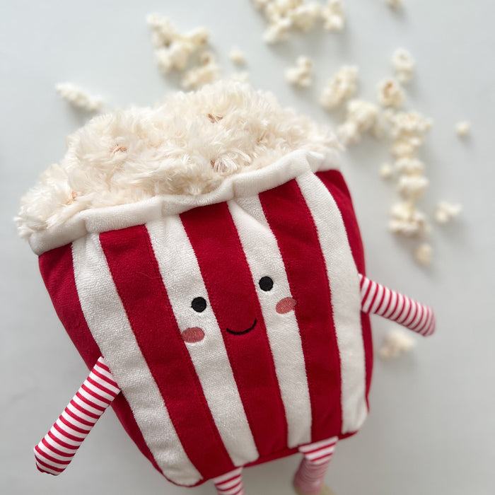 A plush popcorn toy with red and white stripes, a smiling face, and striped arms and legs.