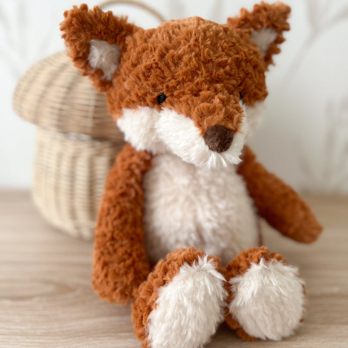 Stuffed fox toy with orange and white fur sitting on a wooden surface.