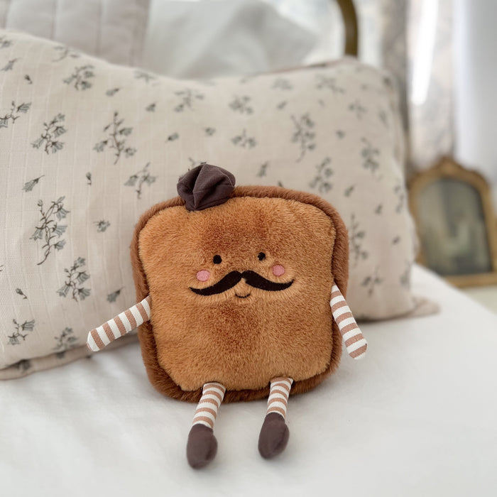 Brown toast plush toy with mustache and hat sitting on a bed.
