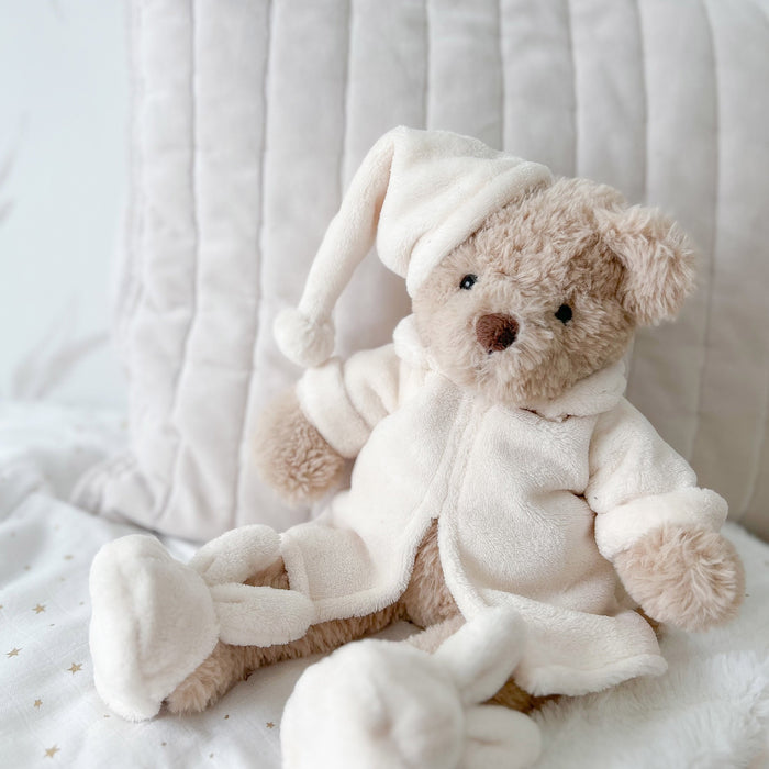 A beige teddy bear wearing pajamas and a sleeping cap.