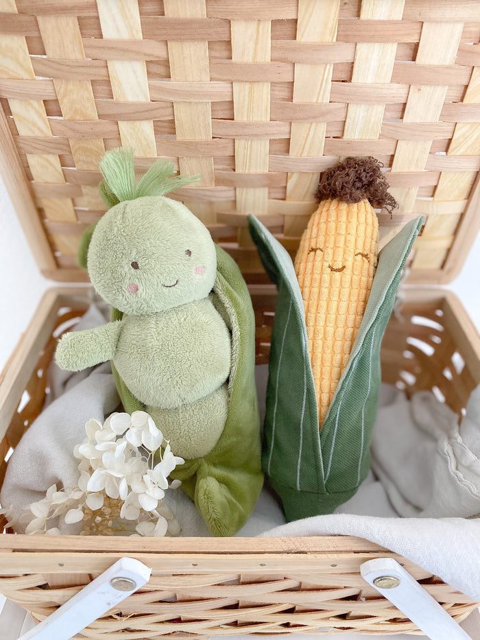 Stuffed toy pea in a pod and corn on the cob in a wicker basket.
