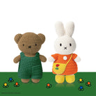 Crocheted Miffy and teddy bear dolls on green background with flowers.