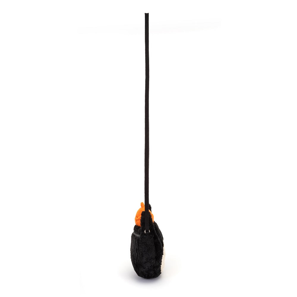 A black and white plush penguin purse with an orange head and a long black strap.