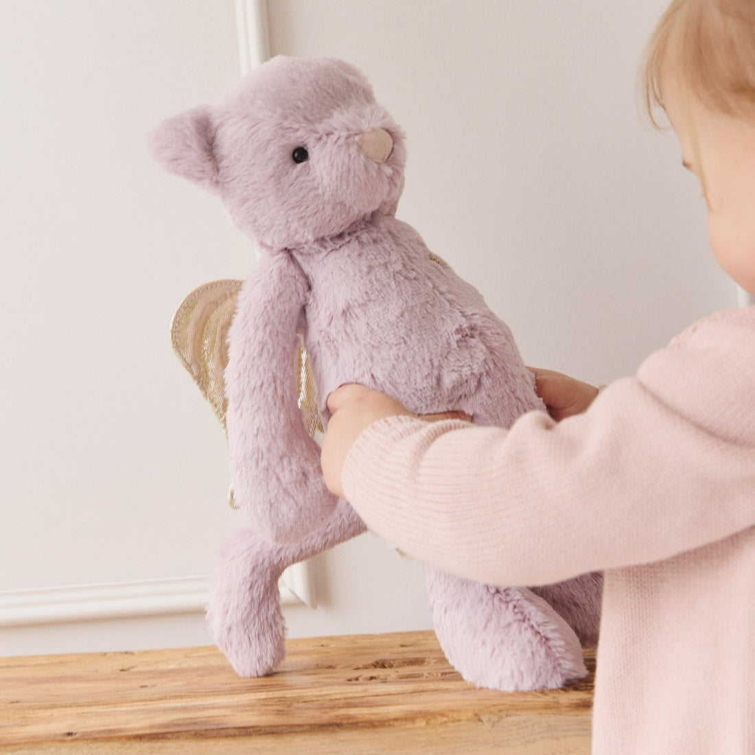 Child holds lilac plush bear with gold wings.