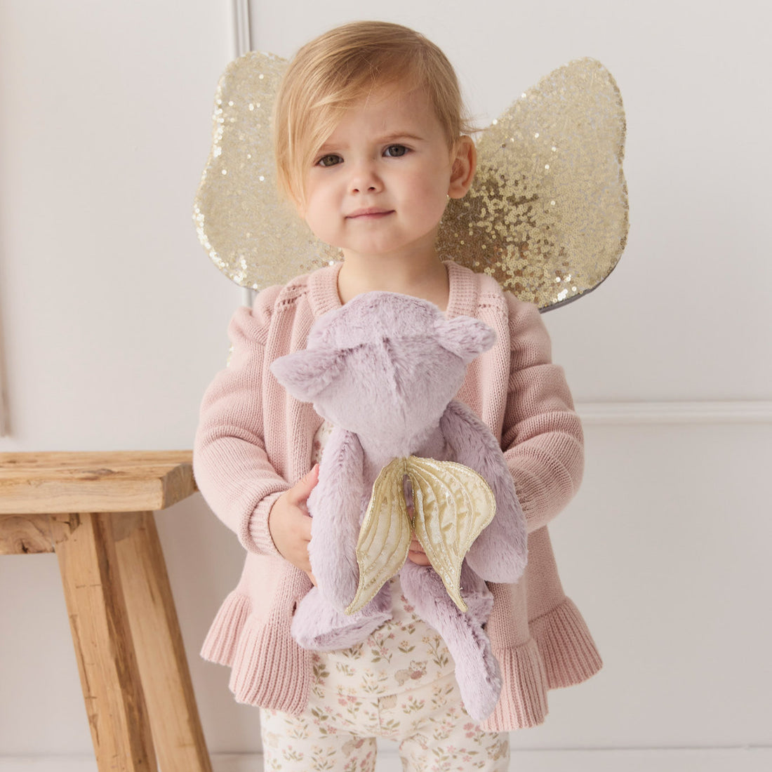 Child with fairy wings holding a plush purple dragon.