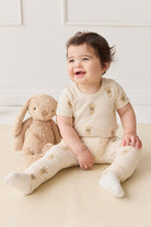 A baby sitting next to a stuffed bunny wearing teddy bear-printed pajamas.