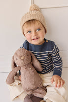 Toddler with a knit hat and sweater holding a stuffed rabbit.