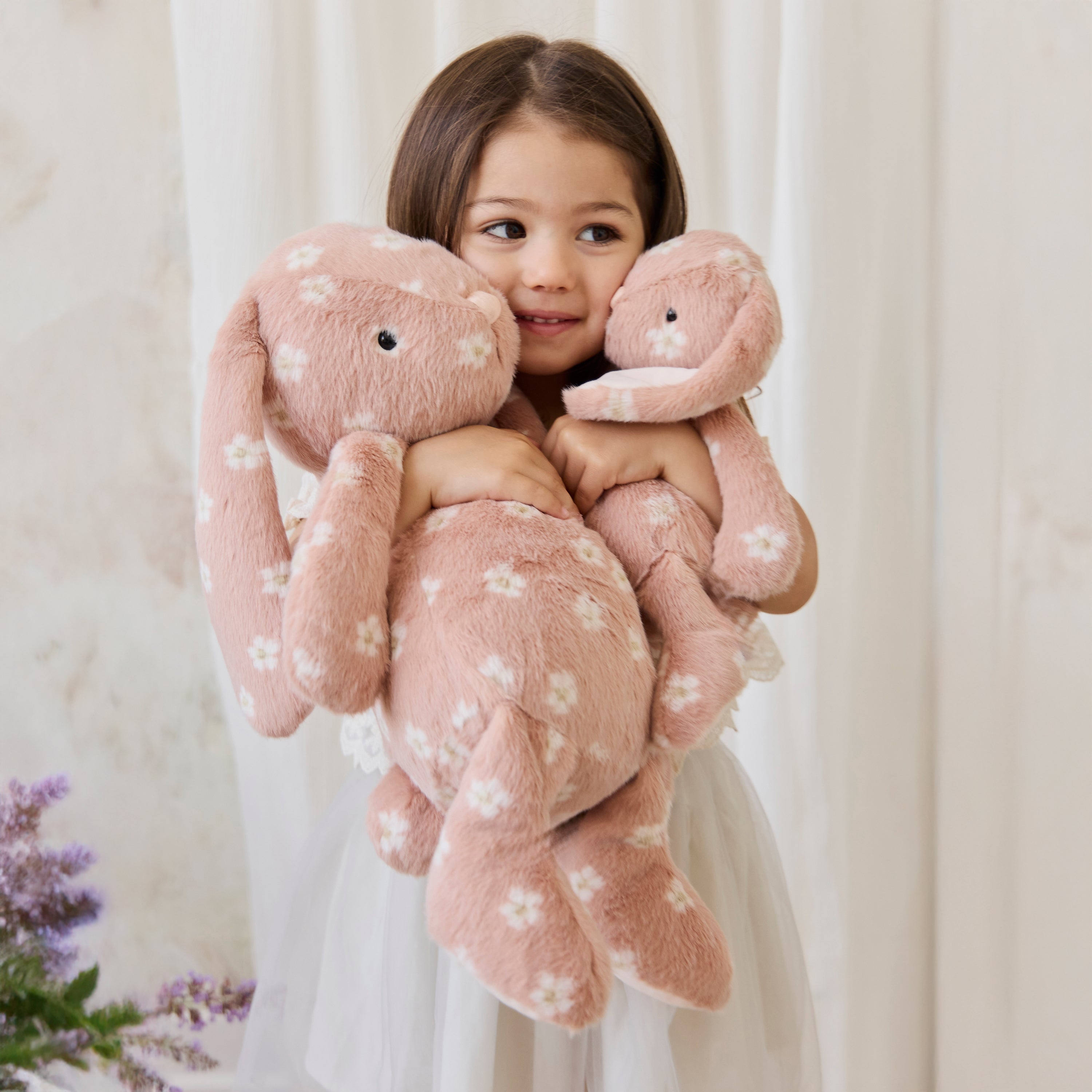 Child holding a large pink plush toy with white floral patterns against a light background