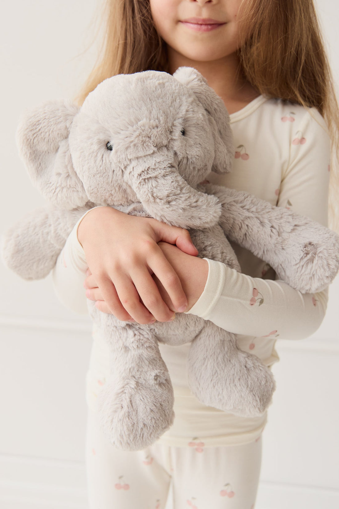 A girl in cherry-print pajamas hugs a gray plush elephant.